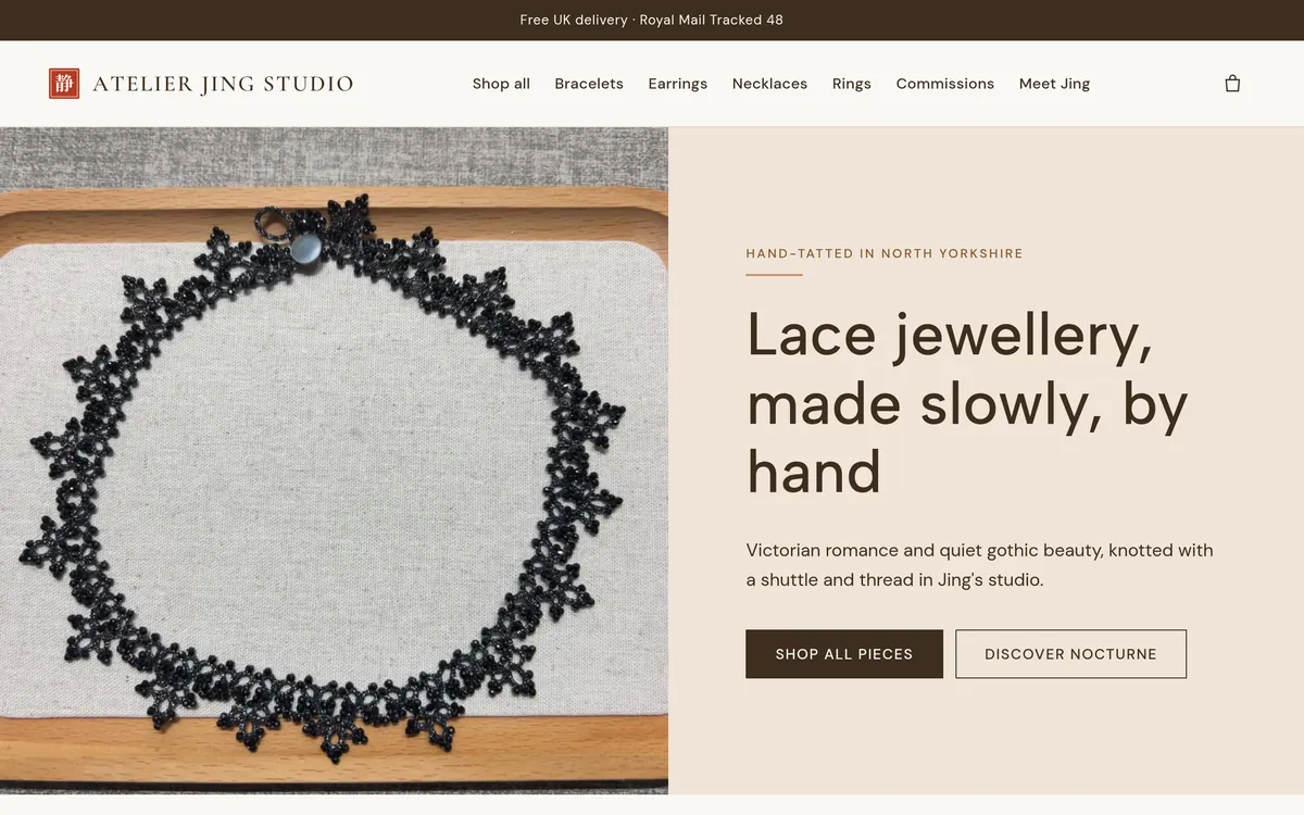 The Atelier Jing Studio shop on a laptop: a black tatted lace collar on a wooden tray, beside the headline "Lace jewellery, made slowly, by hand"